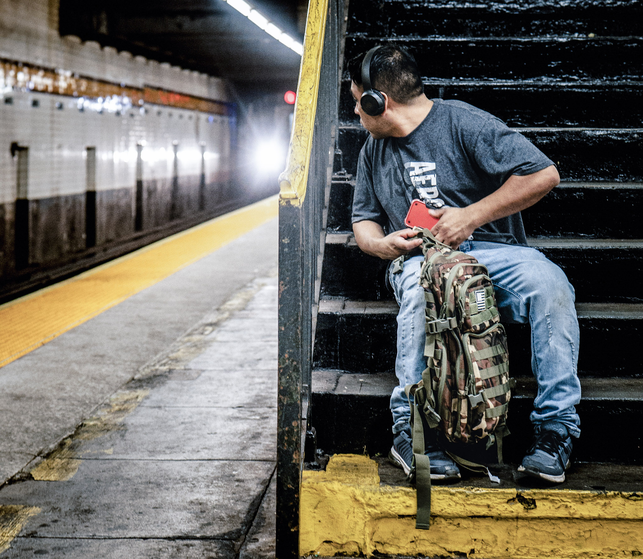 Commuter sitting near a subway platform staircase as a train approaches