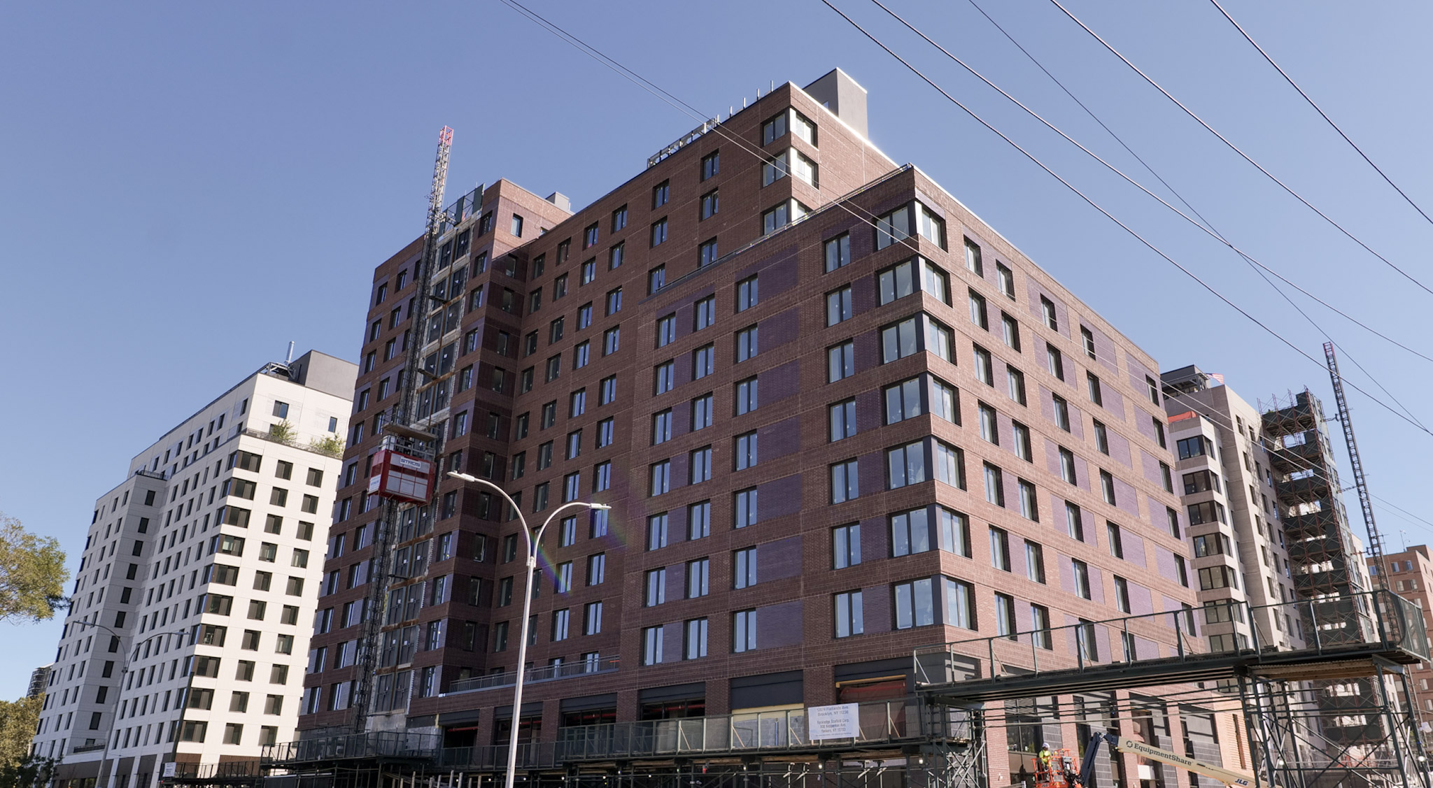 New residential buildings at Innovative Urban Village in East New York, with scaffolding and construction hoists along the street.