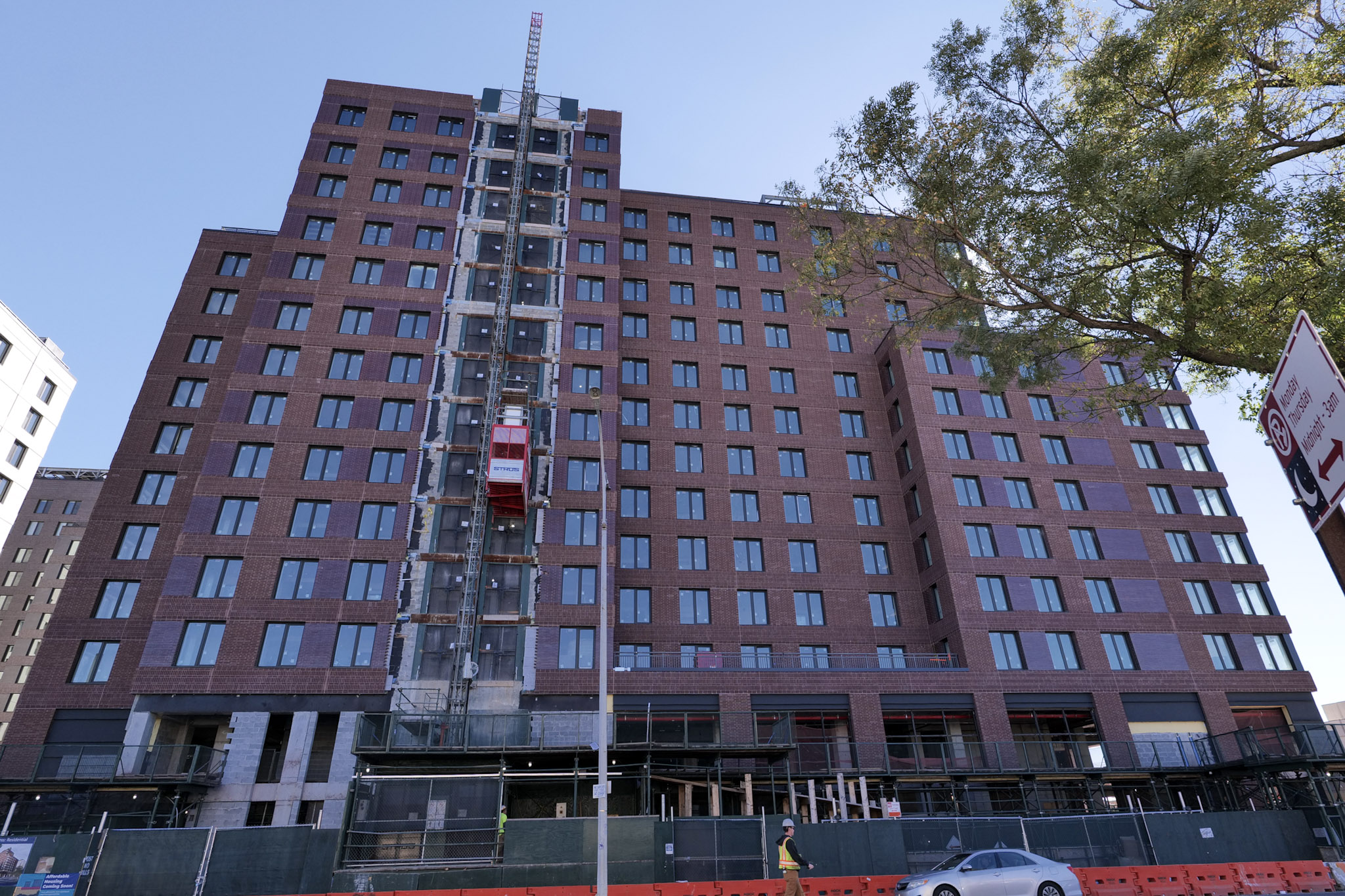 A brick residential building at Innovative Urban Village with an exterior construction hoist, scaffolding and street barriers.