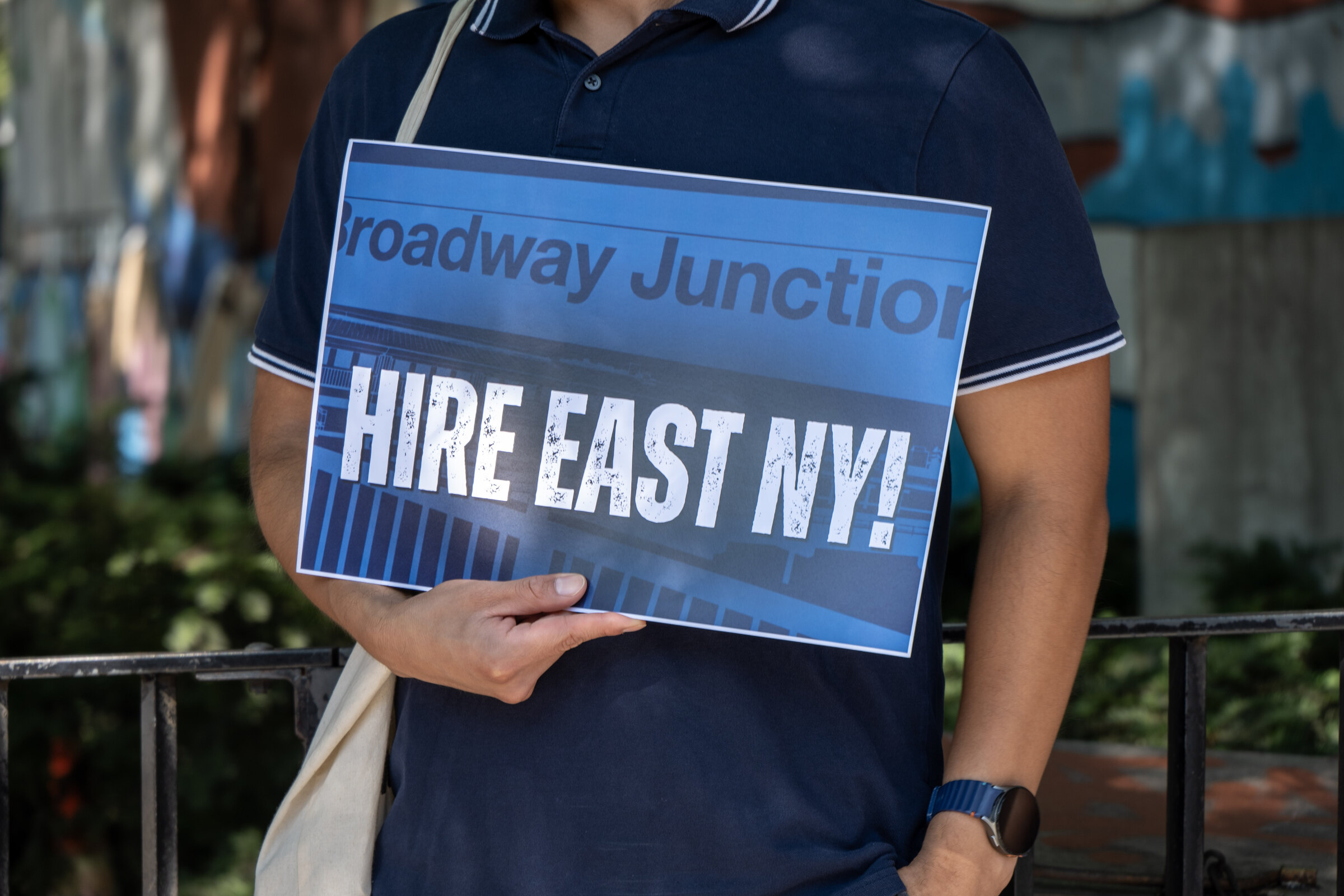 A resident holds a Hire East NY sign at a Broadway Junction local hiring rally