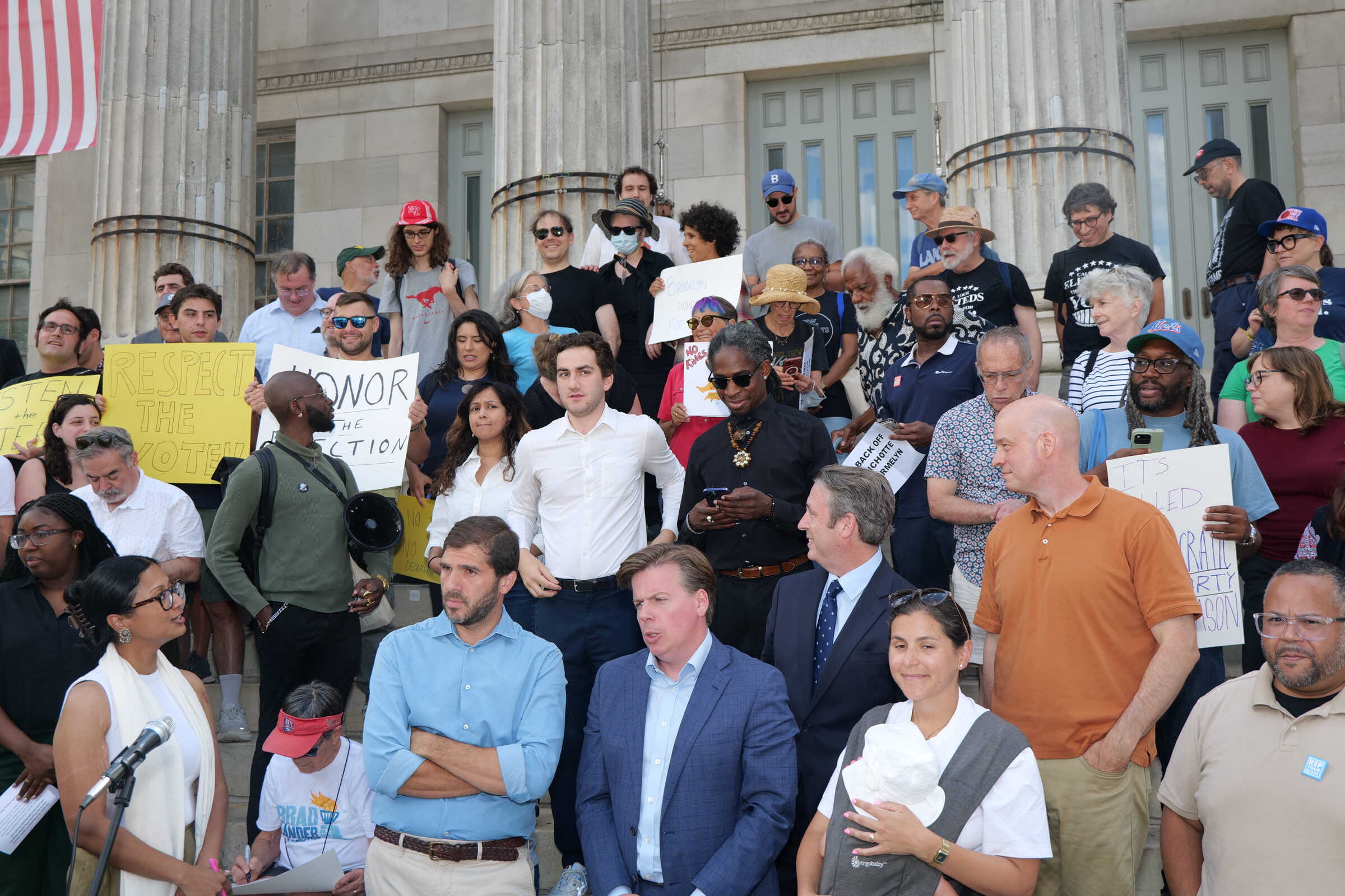 A large crowd of Brooklyn Democrats and supporters stands on the steps of Brooklyn Borough Hall holding hand-lettered signs including “Respect the Voters,” “Honor the Election,” and “Back Off Bichotte Hermelyn.”